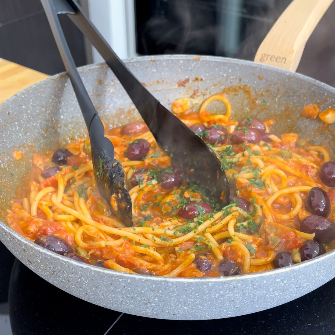 Una padella di spaghetti e olive con le pinze dentro