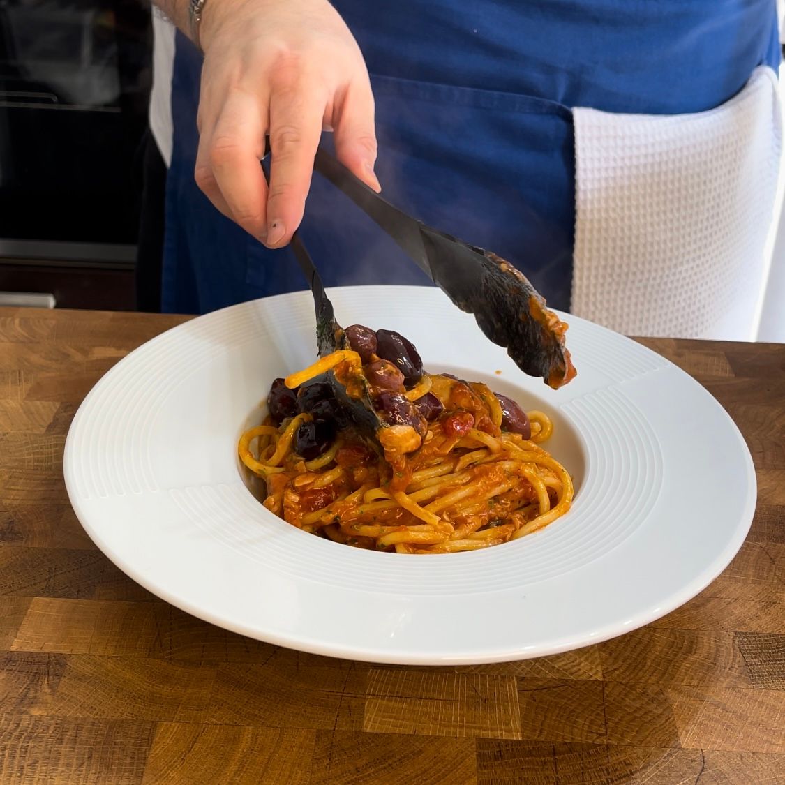 Una persona tiene le pinze sopra un piatto di spaghetti