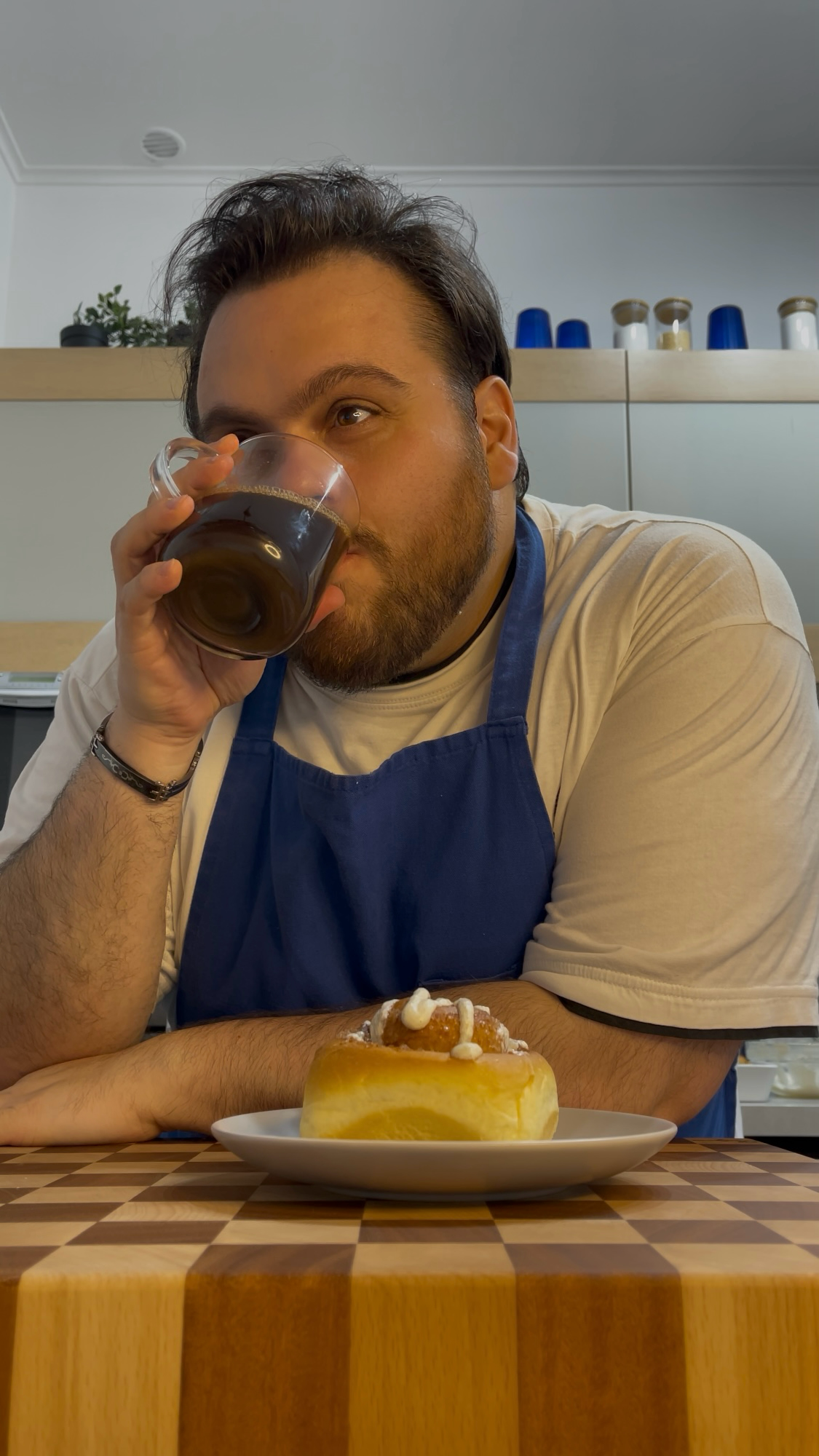 Un uomo beve un bicchiere di caffè mentre è seduto a un tavolo con un piatto di cibo.