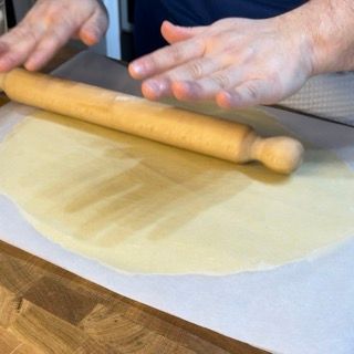 Una persona sta stendendo la pasta con un mattarello di legno