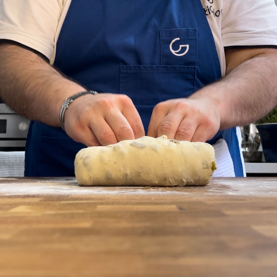 Un uomo con un grembiule blu sta impastando la pasta su un tavolo di legno