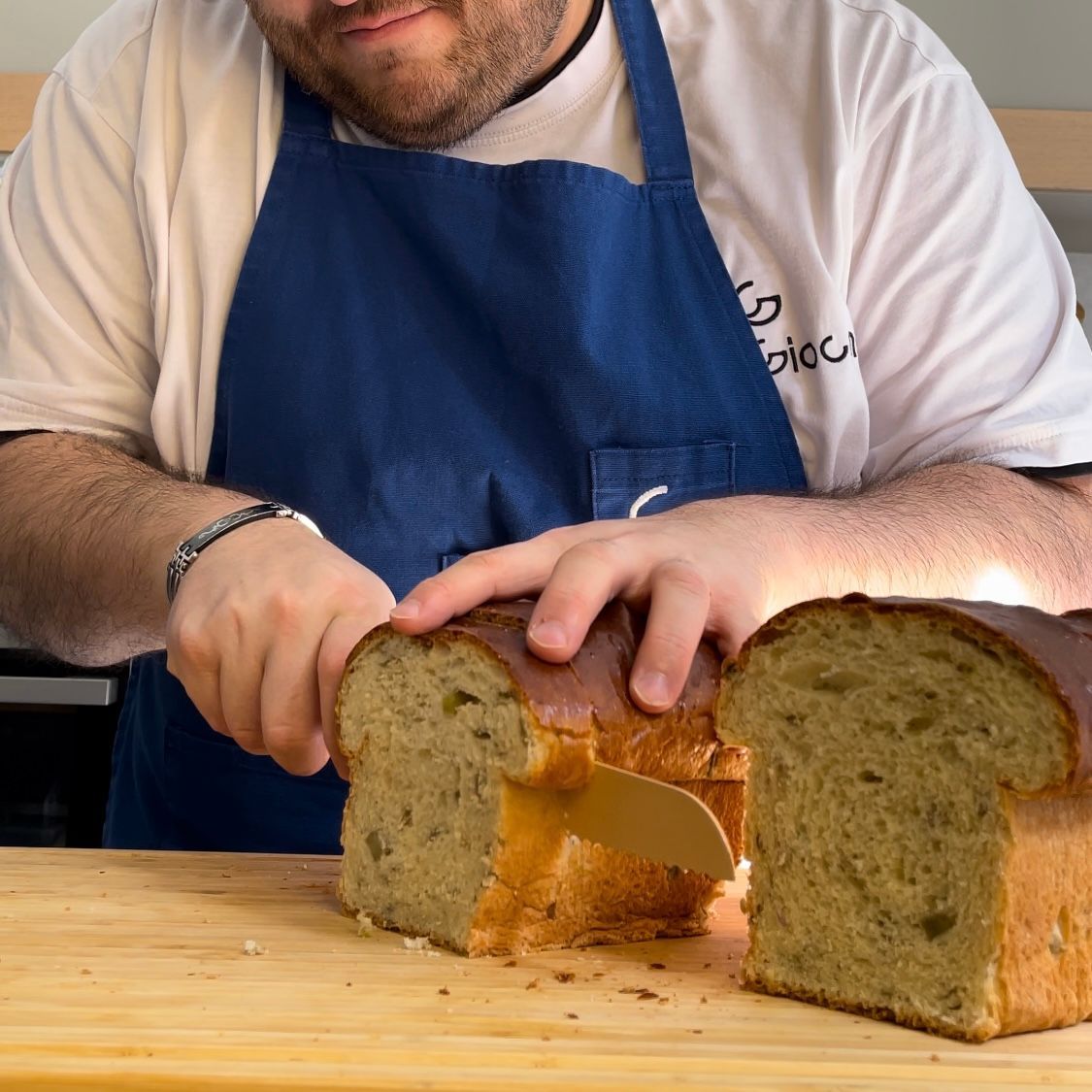 Un uomo con un grembiule sta tagliando una pagnotta di pane su un tagliere