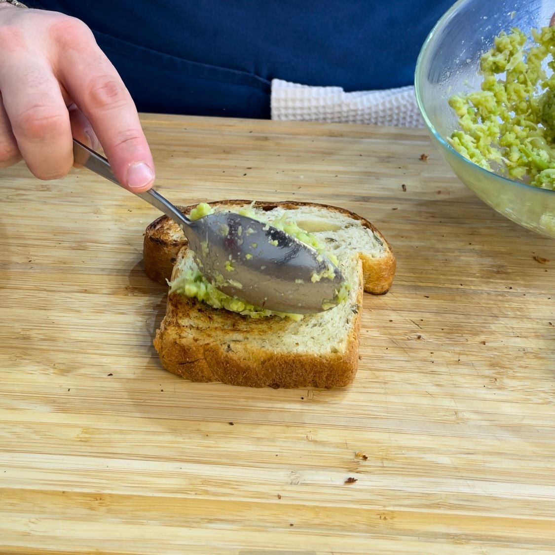 Una persona spalma l'avocado su una fetta di pane con un cucchiaio.