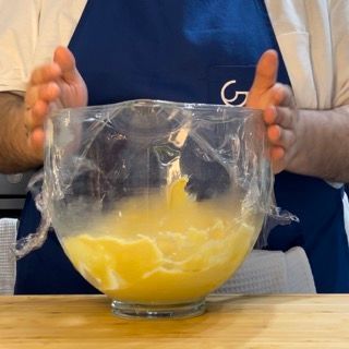 Una persona tiene in mano una ciotola ricoperta di pellicola trasparente
