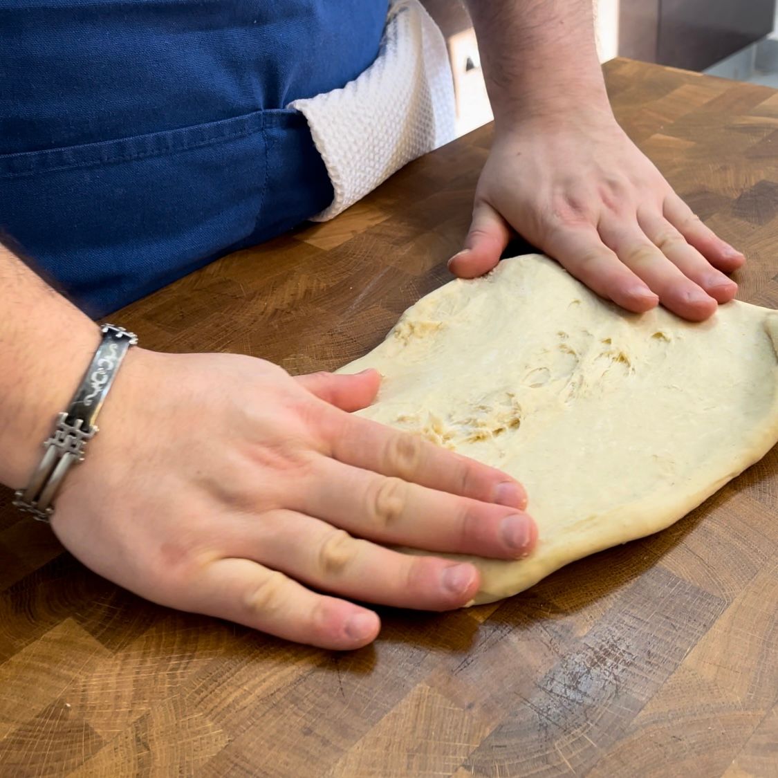 Una persona tiene in mano un pezzo di pasta su un tavolo di legno