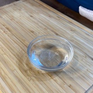 Una piccola ciotola di vetro è appoggiata su un tagliere di legno.