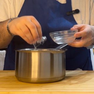 Un uomo con un grembiule sta versando del liquido in una pentola