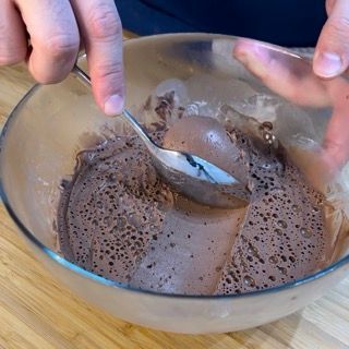 Una persona sta mescolando una ciotola di gelato al cioccolato con un cucchiaio