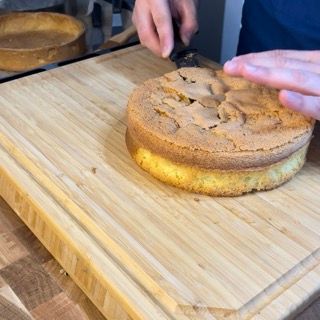 Una persona sta tagliando una torta su un tagliere di legno.