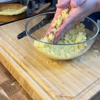 Una persona sta schiacciando le patate in una ciotola di vetro su un tagliere.