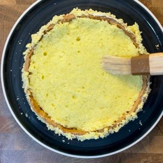 Una torta viene spennellata con una spazzola di legno su un piatto nero