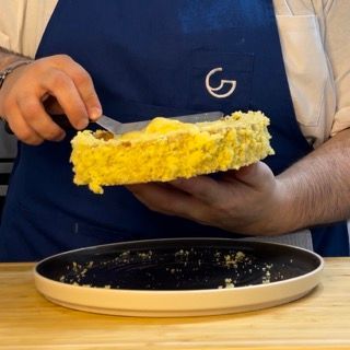 Una persona che indossa un grembiule con la lettera g sopra tiene in mano un pezzo di cibo