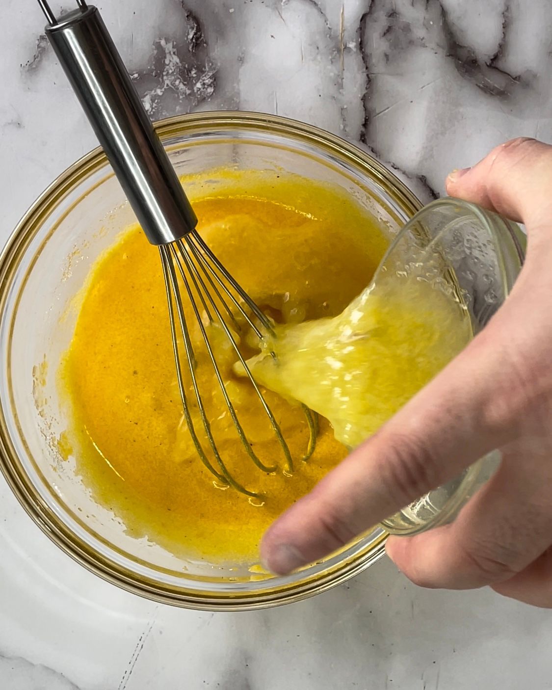 Una persona sta mescolando un liquido giallo in una ciotola di vetro.