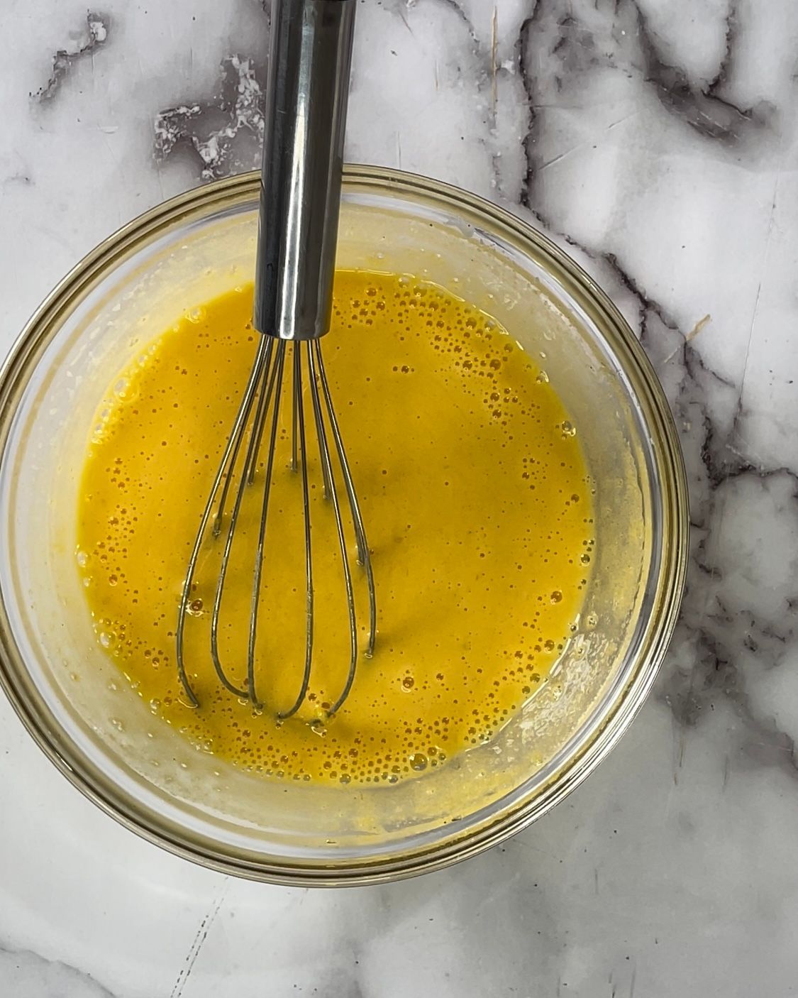 Una ciotola di liquido giallo con una frusta dentro