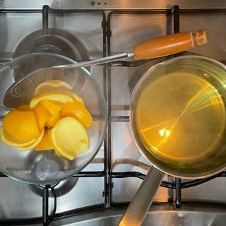 Una ciotola di limoni è appoggiata su un fornello accanto a una pentola di liquido