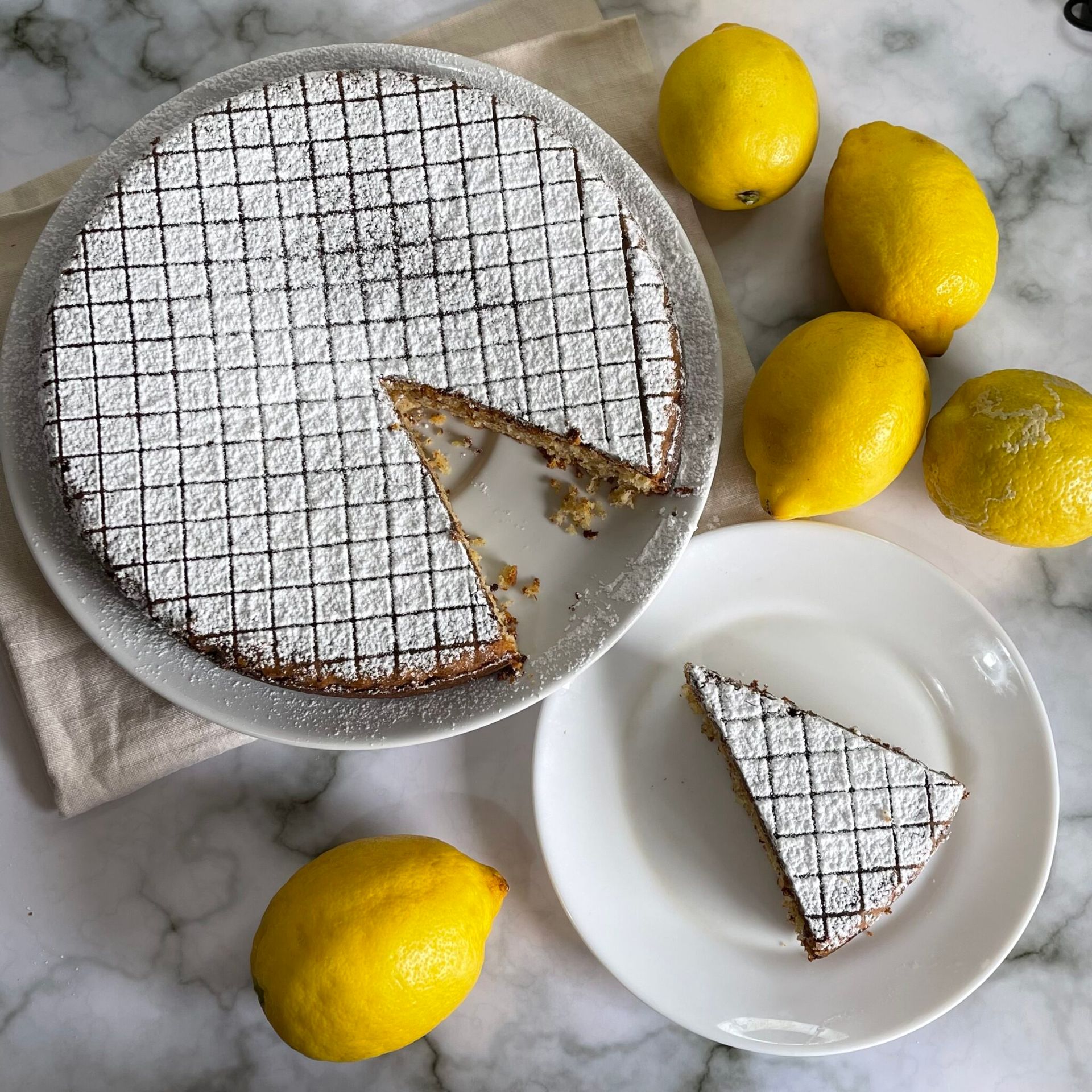Una torta con una fetta staccata si trova su un piatto accanto ai limoni.