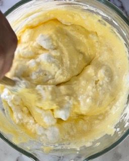 Una persona sta mescolando un liquido giallo in una ciotola di vetro con un cucchiaio di legno.