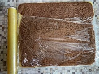 Un pezzo di torta al cioccolato avvolto in pellicola trasparente accanto a un rotolo di pellicola trasparente.