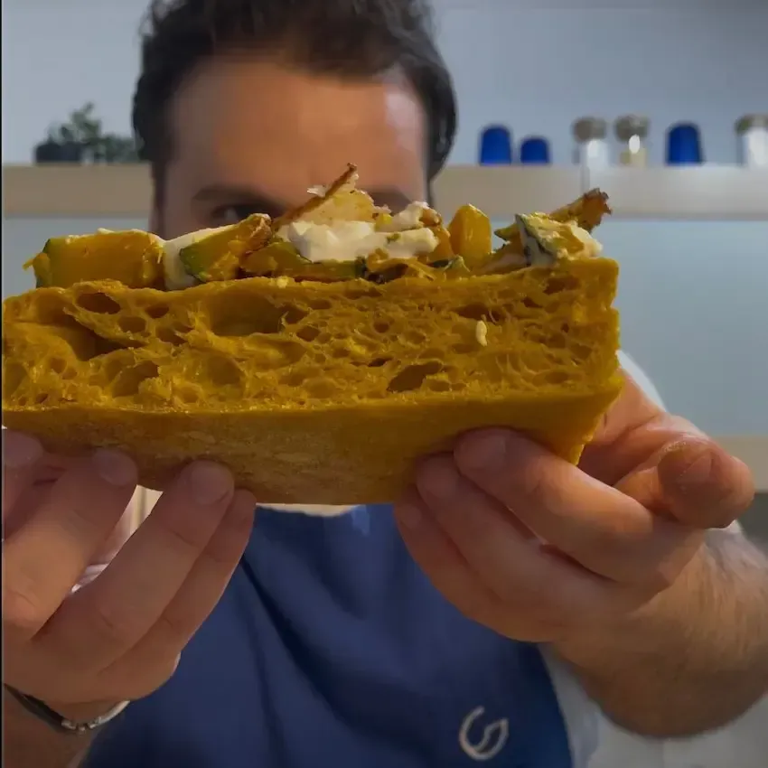 Trancio di pizza alla zucca che mostra la burrata filante, l'impasto soffice e il guanciale saporito.