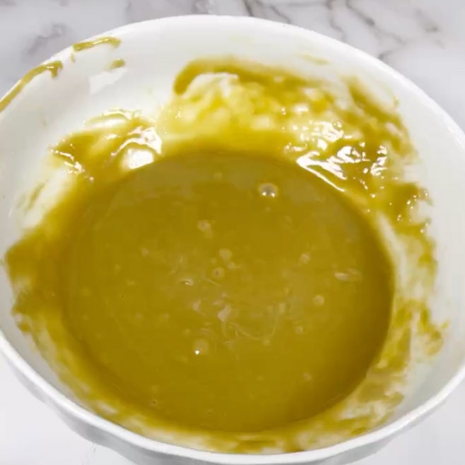 Una ciotola bianca piena di un liquido giallo su un tavolo.
