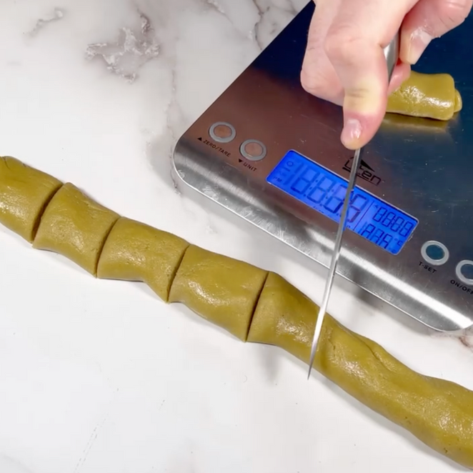 Una persona sta tagliando un pezzo di pasta su una bilancia che indica 88,7
