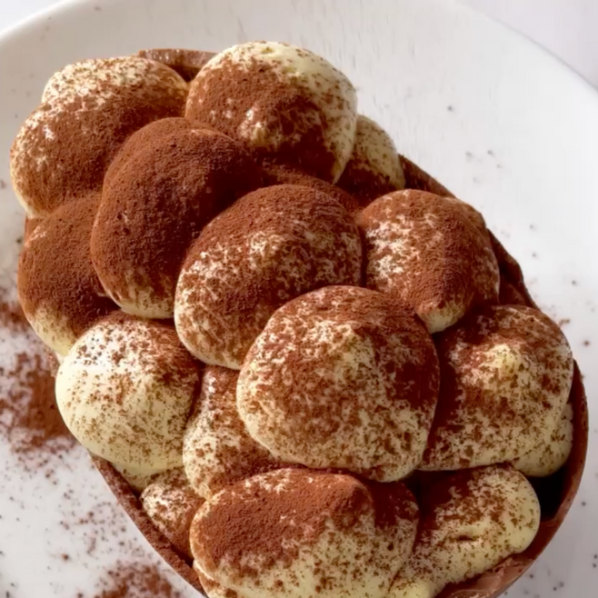 Un piatto bianco sormontato da un uovo di cioccolato ripieno di tiramisù