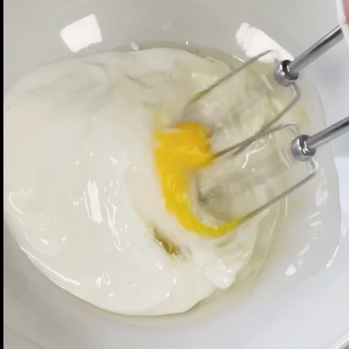 Una persona sta mescolando un uovo giallo in una ciotola di yogurt.