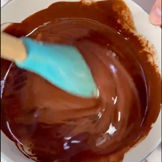 Una persona sta mescolando una ciotola di cioccolato con una spatola blu