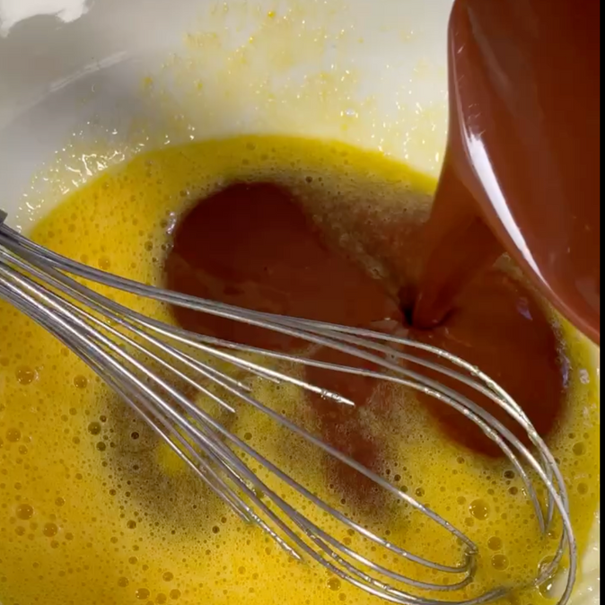 Un liquido marrone viene versato in un liquido giallo con una frusta