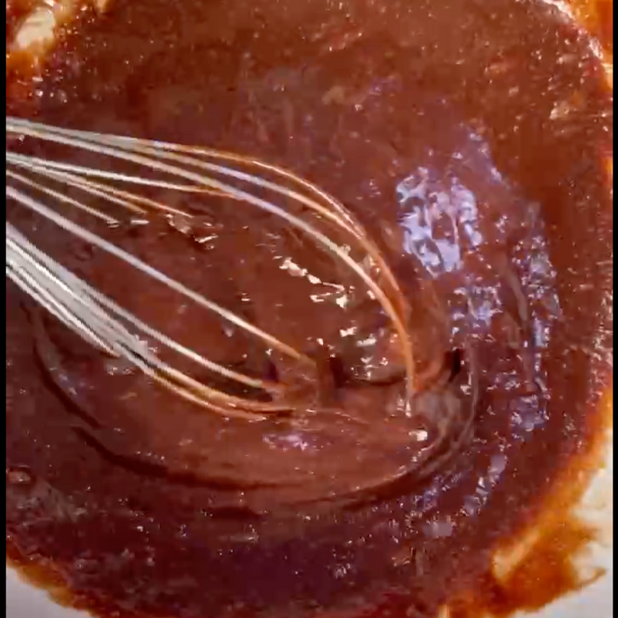Primo piano di una frusta in una ciotola di salsa al cioccolato.