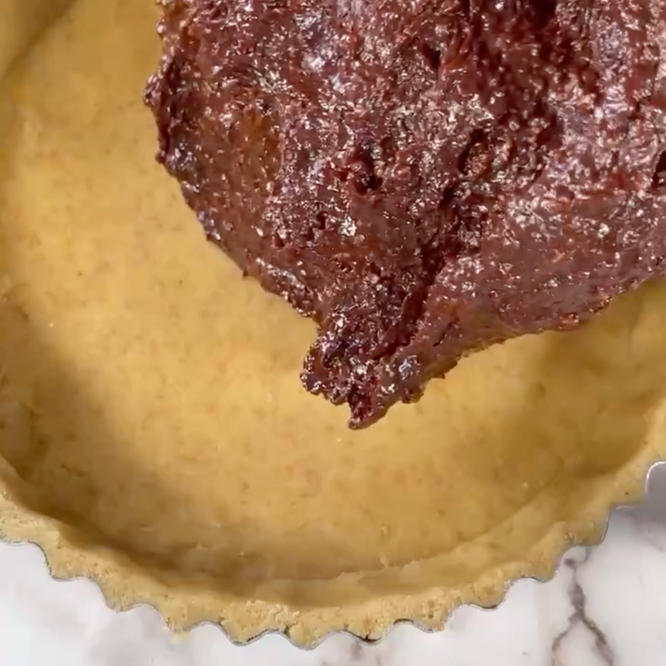 Primo piano di una persona che versa il cioccolato nella base di una torta.