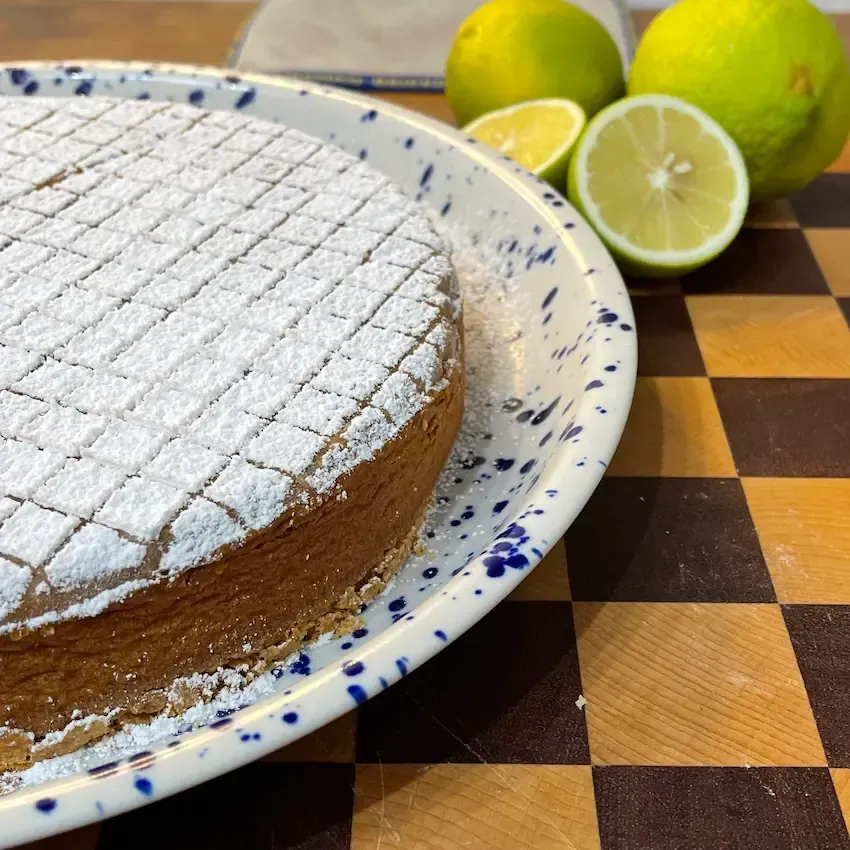 Torta caprese al limone intera spolverata di zucchero a velo e limone. Una caprese bianca morbida e umida ricetta originale.