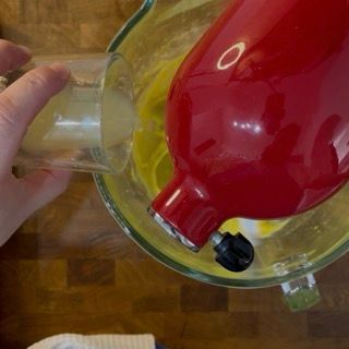 Inserimento dei tuorli d'uovo uno alla volta nella crema profumata per la torta caprese al limone.