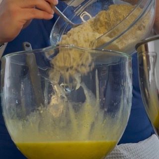 Aggiunta del primo terzo di polveri secche al composto di tuorli per la caprese al limone ricetta.