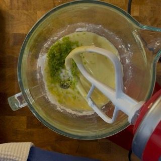 Versamento dell'olio di semi e dello zucchero a velo nella ciotola con la scorza grattugiata di limone.