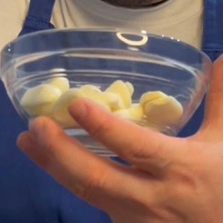 Rimozione della pelle esterna dagli spicchi d'aglio freschi su un tagliere per la ricetta crema di aglio.