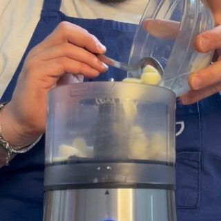 Trasferimento degli spicchi d'aglio stracotti e profumati nel contenitore di un cutter da cucina