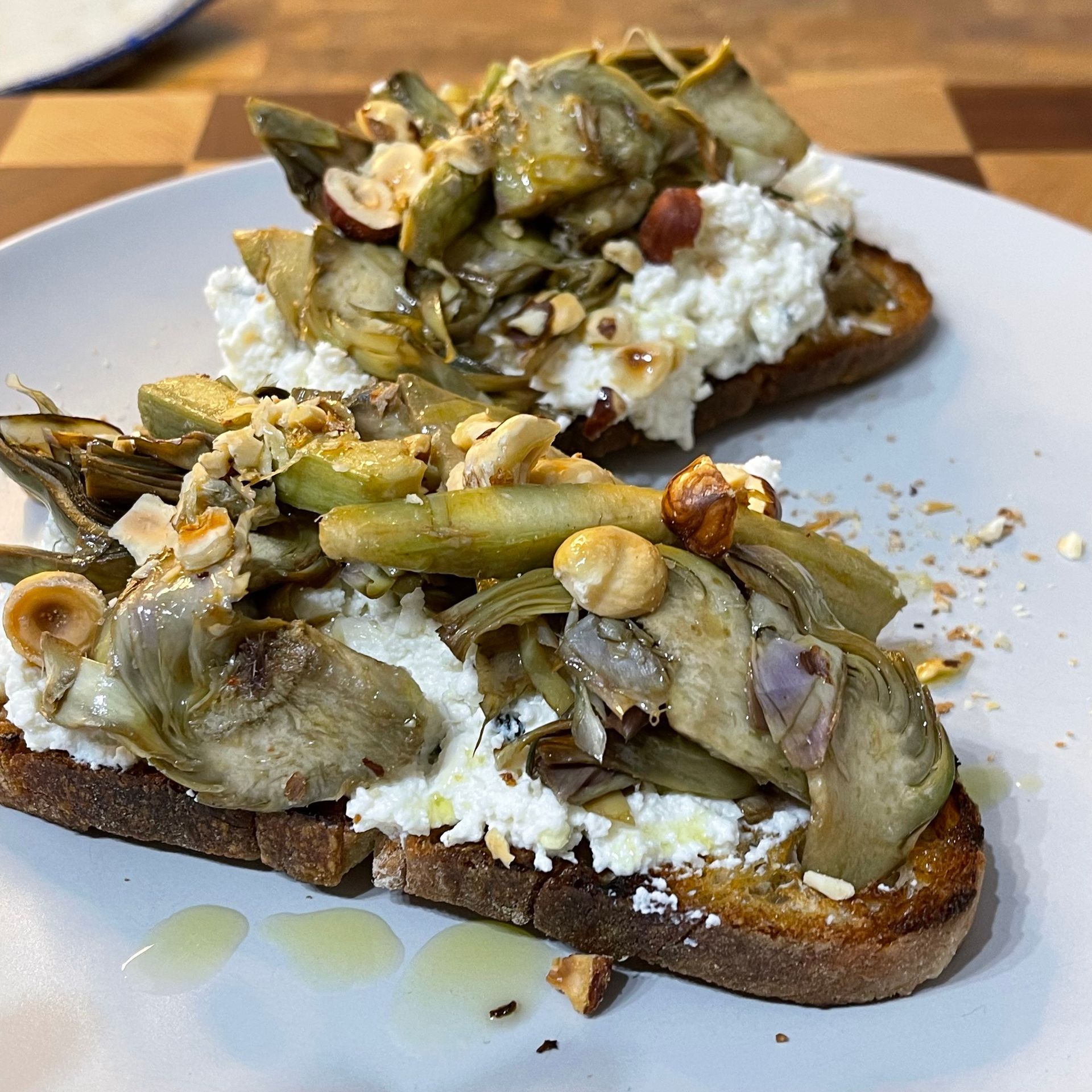 Due fette di pane tostato con carciofi e formaggio su un piatto bianco