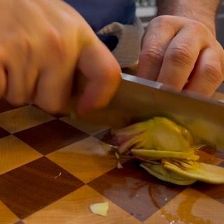 Una persona sta tagliando un carciofo su un tagliere