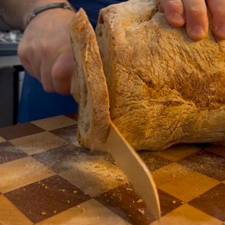 Una persona sta tagliando una pagnotta di pane su un tagliere
