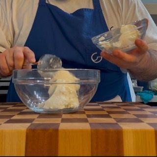 Un uomo con un grembiule blu sta mescolando qualcosa in una ciotola di vetro