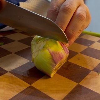 Una persona sta tagliando un carciofo su un tagliere a scacchi
