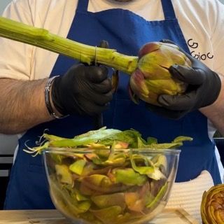 Un uomo con un grembiule blu sta sbucciando i carciofi