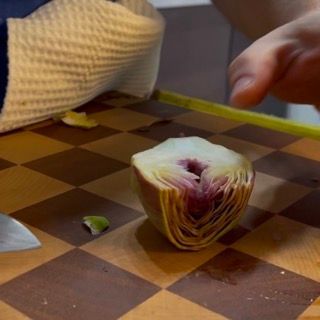 Una persona sta tagliando un carciofo su un tagliere a scacchi