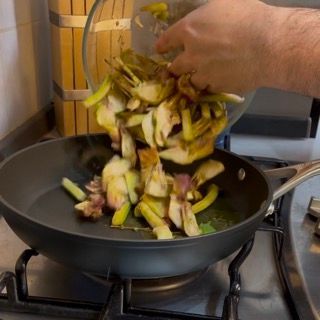 Una persona sta versando le verdure in una padella sul fornello