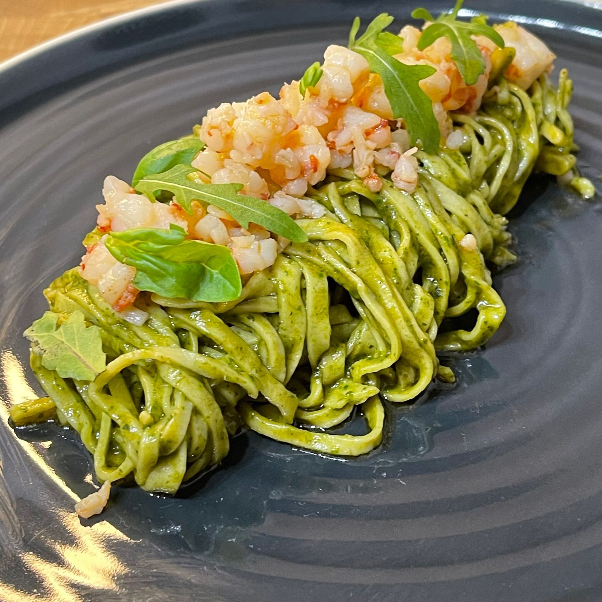 Un piatto nero con sopra tagliatelle verdi e gamberi