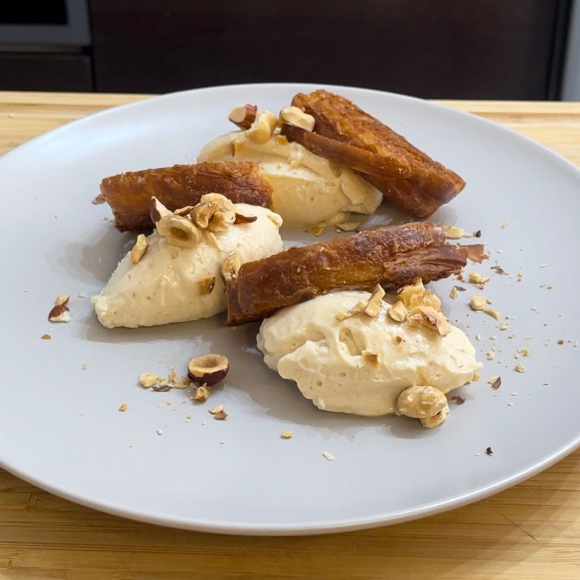 Un piatto bianco con sopra gelato e noci su un tavolo di legno.