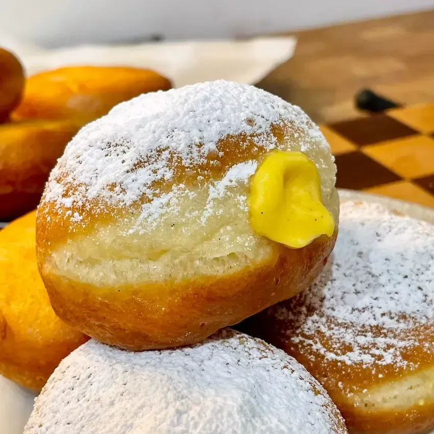 Krapfen alla crema appena fritti, dorati e spolverati di zucchero a velo.