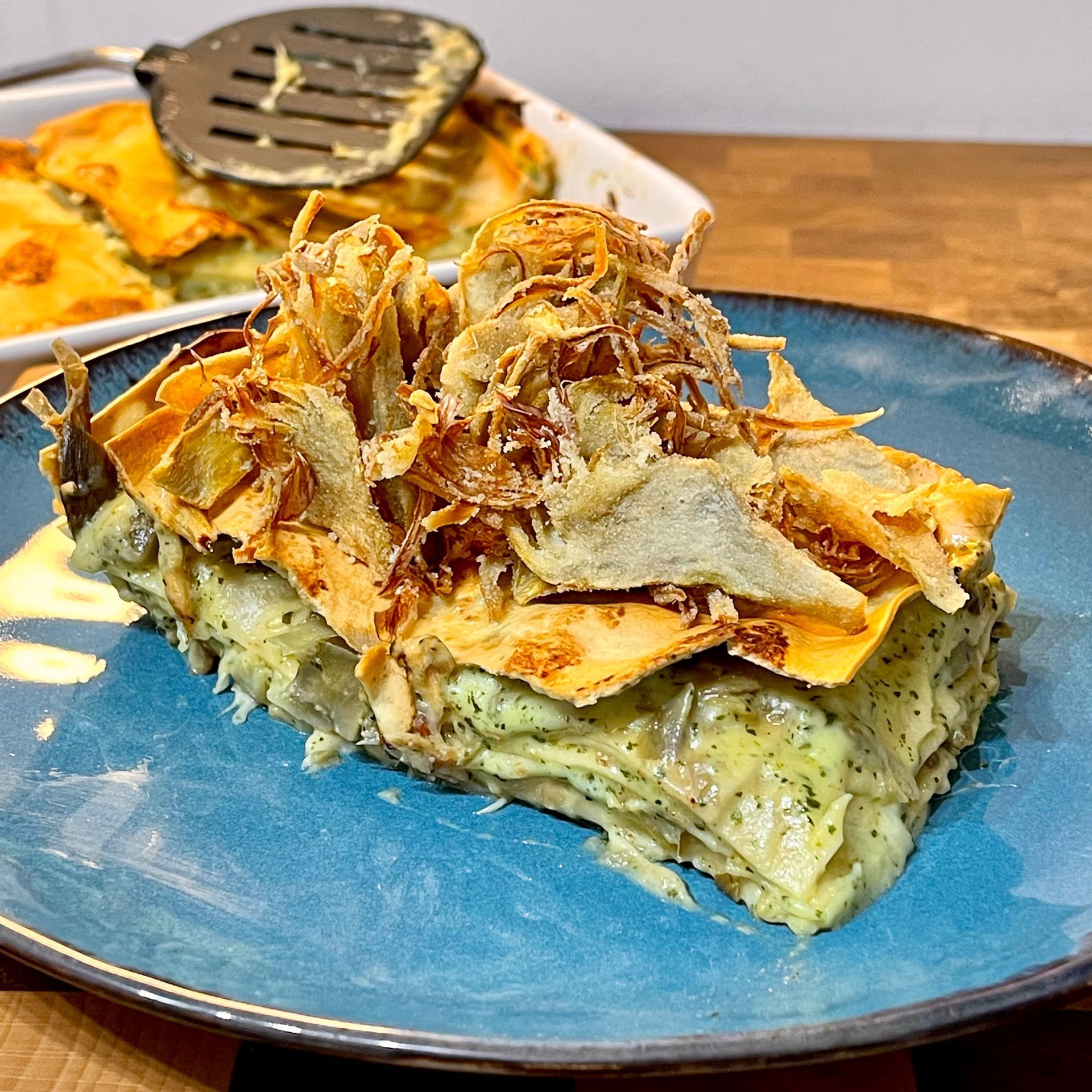 Una fetta di lasagna è su un piatto blu su un tavolo di legno.