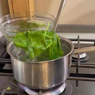 Foglie di basilico scolate dopo 10 secondi e immerse nell'acqua e ghiaccio per l'olio al basilico ricetta veloce.